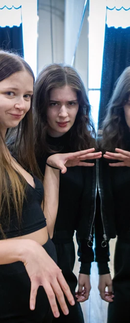 Two female students and their reflections in a mirror, posing with playful hand gestures and smiles in a dance studio filled with natural light Two female students and their reflections in a mirror, posing with playful hand gestures and smiles in a dance studio filled with natural light
